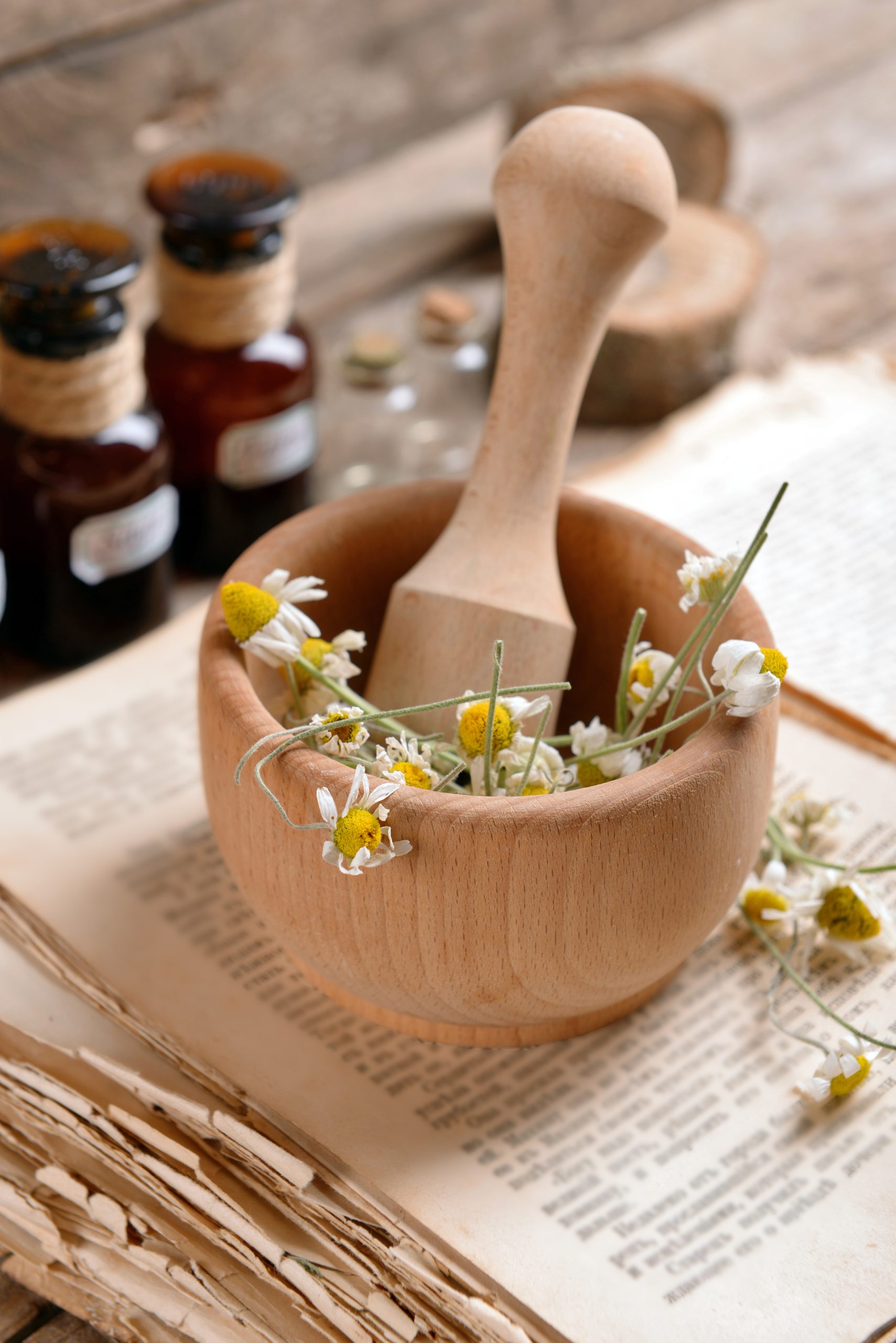 Old book with dry flowers in mortar and bottles on table close up